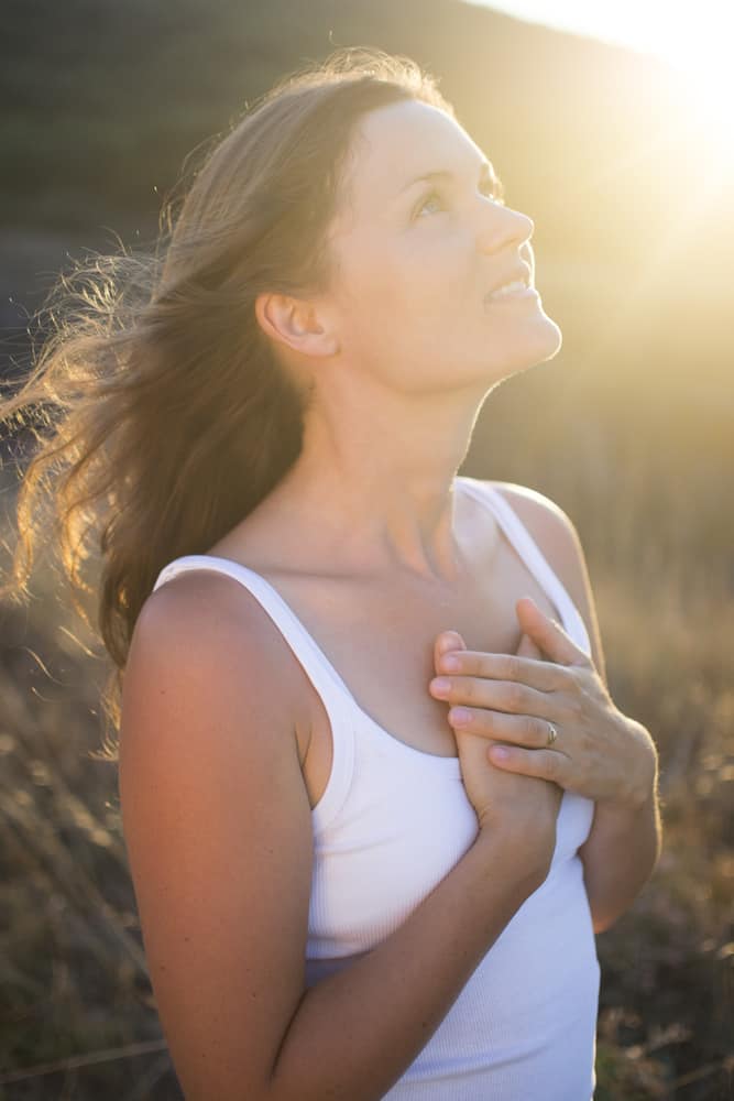 Beautiful young woman with her hands on her chest looking gratefully towards the sky.