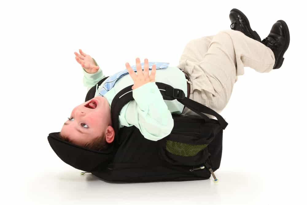 Adorable 3 year old child knocked backwards from a heavy back pack over white background.