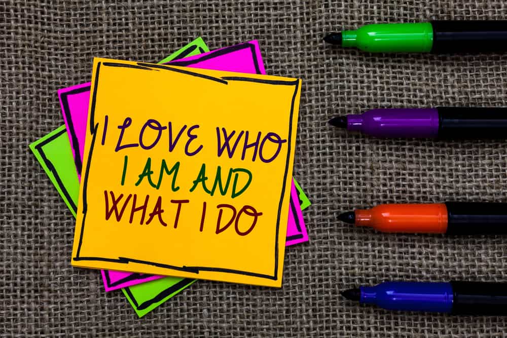 Text sign showing I Love Who I Am And What I Do. Conceptual photo High self-stem being comfortable with your job Written on some colorful sticky note 4 pens laid in rank on jute base