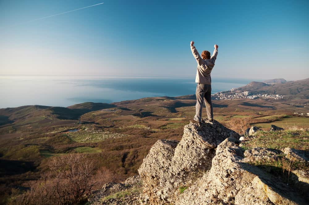 On the top of world, man standing on a rock. His arms is up to sky.
