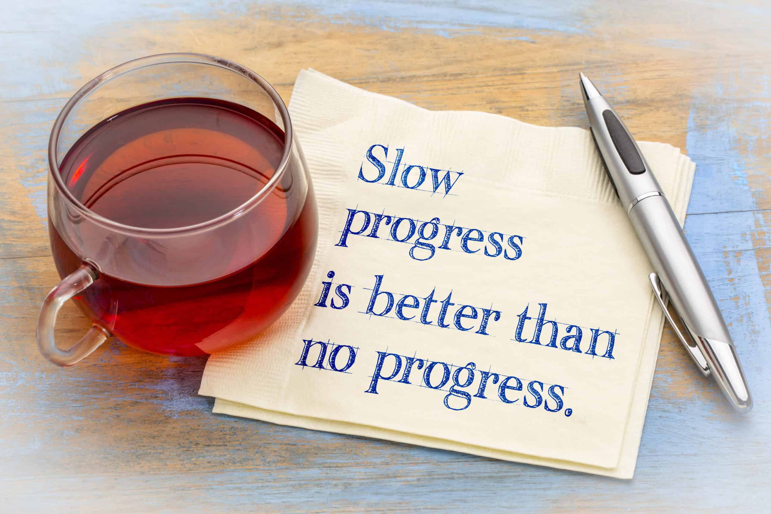 Slow progress is better than no progress inspirational note - handwriting on a napkin with a cup of coffee